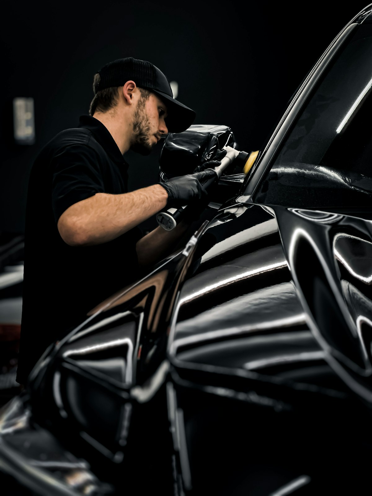 A detailer polishing the black paint of a car with a machine polisher